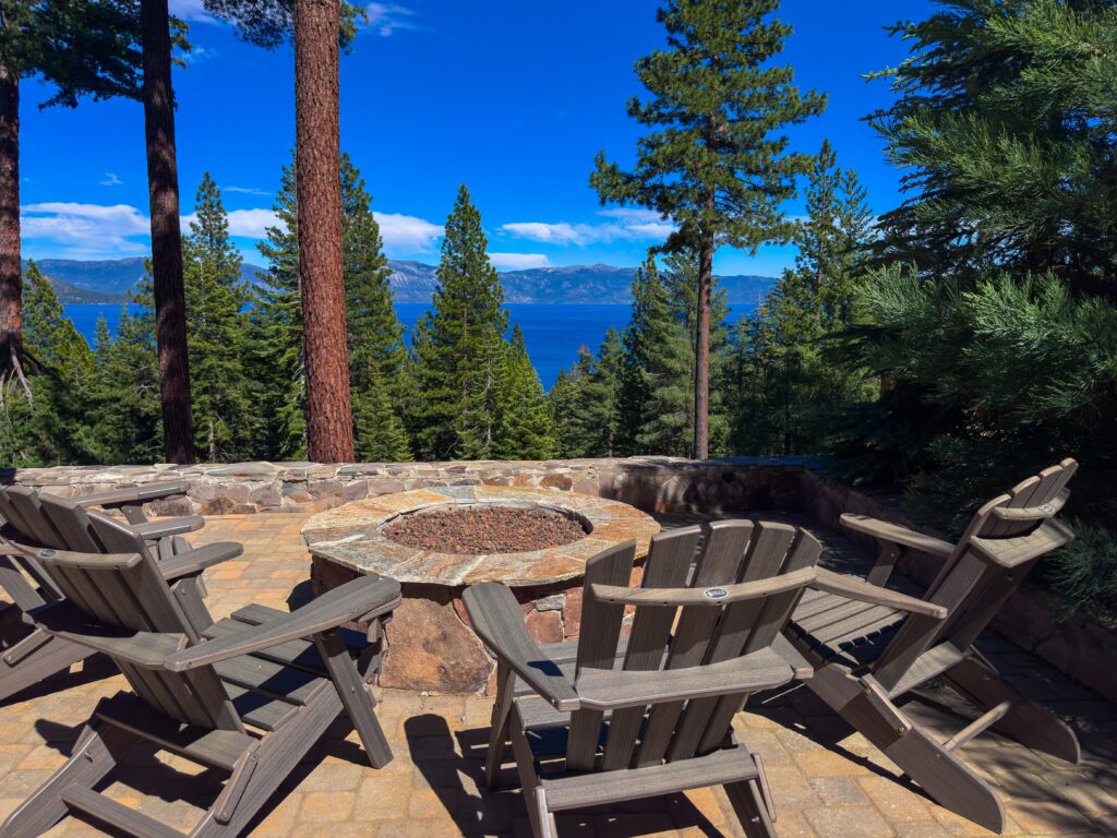 Lake Tahoe Luxury Outdoor Living with Panoramic Lake Views Stone patio with a fire pit and Adirondack chairs overlooking Lake Tahoe through tall pine trees